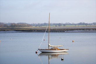 One yacht moored off muddy shore calm water River Deben, Waldringfield, Suffolk, England, UK