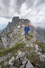 Mountaineer with helmet on a narrow hiking trail on a rocky ridge, ascent to the Maukspitze, clouds