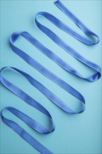 Blue ribbon on a blue pastel background. Celebration concept. Top view, close up, flat lay