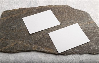 White paper business card, mockup with natural stone on gray concrete background. Blank, side view,