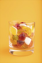 Various fruit jelly candies in drinking glass on orange pastel background. side view, close up