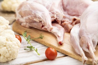 Whole raw rabbit with cauliflower, tomatoes and spices on a white wooden background and linen