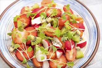 Vegetarian fruits and vegetables salad of strawberry, kiwi, tomatoes, microgreen sprouts on white