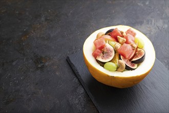 Vegetarian fruit salad of watermelon, grapes, figs, pear, orange, cashew on slate board on a black