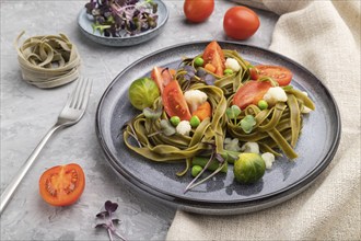 Tagliatelle green spinach pasta with tomato, pea and microgreen sprouts on a gray concrete