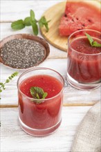 Watermelon juice with chia seeds and mint in glass on a white wooden background with linen textile.