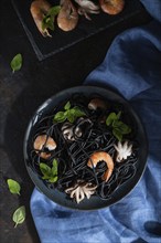 Black cuttlefish ink pasta with shrimps or prawns and small octopuses on black concrete background