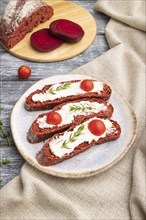 Red beet bread sandwiches with cream cheese and tomatoes on gray wooden background and linen