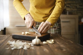 Unrecognizable man chopping garlic with knife on wooden cutting board