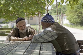 Two bearded elderly men wearing traditional taqiyah having a cup of tea on the main square of a