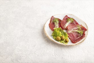 Slices of smoked salted meat with cilantro microgreen on gray concrete background. Side view, copy