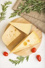 Various types of cheese with rosemary and tomatoes on wooden board on a white wooden background and