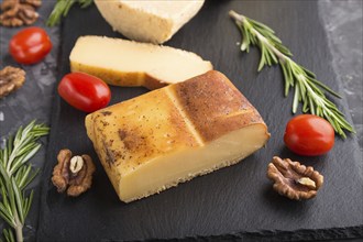 Smoked cheese and various types of cheese with rosemary and tomatoes on black slate board on a