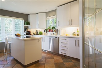 White cabinets, quartz countertop and island with glass cooktop and high back bar stool in kitchen