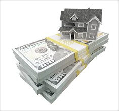 Miniature house resting on stack of thousands of dollars cash isolated on a white background