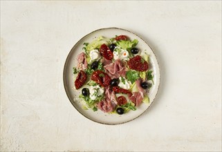 Salad with dried tomatoes, prosciutto, soft cheese, olives, homemade, top view