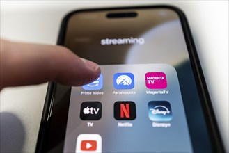 One finger touches the Prime Video app icon on a smartphone screen with various other streaming