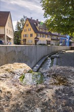 Close-up of a fountain with running water, historic houses in the background. Peaceful atmosphere,