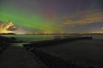 Northern Lights over a sea with distant city lights and partly cloudy sky, beach, Tönsberg,