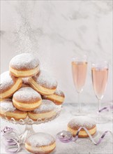 Doughnuts on a glass stand with rosé sparkling wine in the background and falling icing sugar