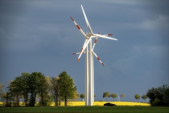 Wind turbines on a rape field, dark rain clouds, in the Rhenish lignite mining area, country road,