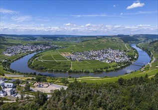 Panoramic view of a winding river surrounded by vineyards and a village with blue sky and clouds in