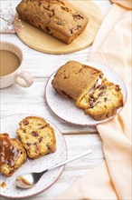 Homemade cake with raisins, almonds, soft caramel and a cup of coffee on a white wooden background