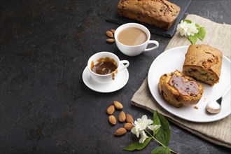 Homemade cake with raisins, almonds, soft caramel and a cup of coffee on a black concrete