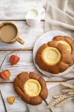 Sour cream bun with cup of coffee on a white wooden background and linen textile. top view, flat