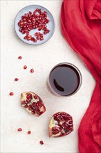 Glass of pomegranate juice on a white concrete background with red textile. Top view, close up,