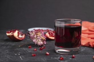 Glass of pomegranate juice on a black concrete background with red textile. Side view, close up,