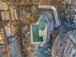 An aerial view of a swimming pool surrounded by streets and trees in winter with frozen water, ENCW