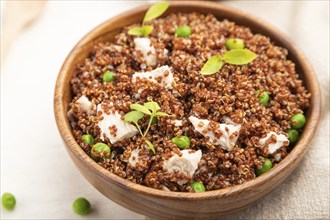 Quinoa porridge with green pea and chicken in wooden bowl on a white wooden background and linen