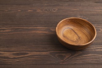 Empty brown wooden bowl on brown wooden background. Side view, copy space