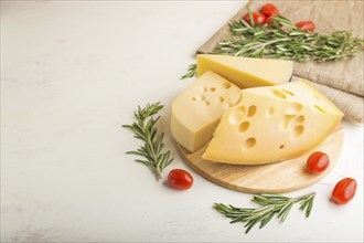 Various types of cheese with rosemary and tomatoes on wooden board on a white wooden background and