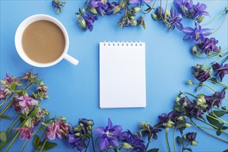 Pink and purple columbine flowers and a cup of coffee with notebook on pastel blue background.