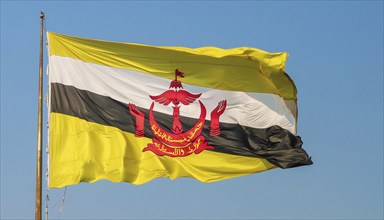 The flag of Brunei flutters in the wind, isolated against a blue sky