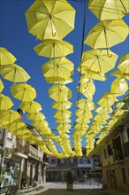 A street under a sky of yellow umbrellas that form an artistic installation on a sunny day,