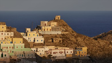 Cluster of houses on a hill overlooking the sea, warm colours and light morning light, Colourful