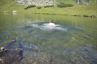 Hiker swimming in the ice-cold mountain lake Mittlerer Kaltenbachsee, Sölktäler Nature Park,