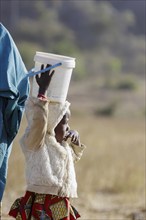 Very small girl carrying a heavy bucket of water on her head, Maraban Dare, 07/02/2024