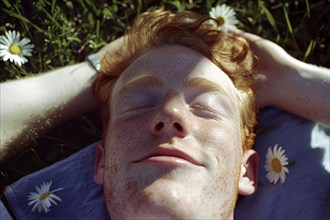 Teenager, young fair-skinned man with red hair and freckles lying on a spring meadow and basking in