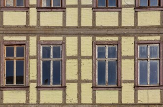 Façade of a historic half-timbered building with yellow walls and several rectangular windows with