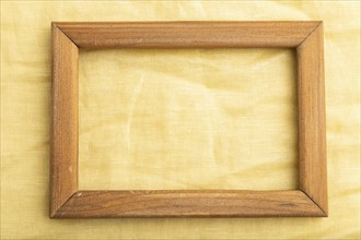 Wooden frame on smooth yellow linen tissue. Top view, flat lay, natural textile background and