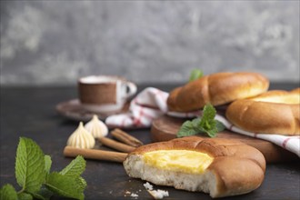 Sour cream bun with cup of coffee on a black concrete background and linen textile. Side view,