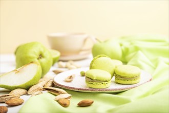 Green macarons or macaroons cakes with cup of coffee on a white wooden background and green linen