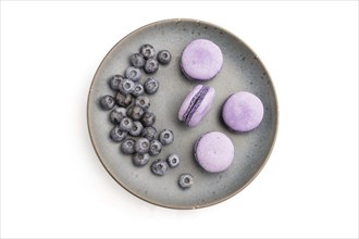 Purple macarons or macaroons cakes with blueberries on ceramic plate isolated on white background.