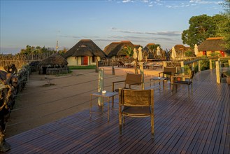 Sunset over African lodge with thatched roof huts and wooden terrace in the foreground, Namibia,