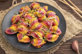 Rainbow colored dumplings with pepper, herbs, microgreen on brown wooden background and linen