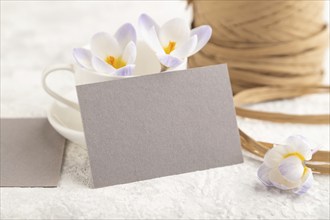 Gray paper invitation card, mockup with purple crocus snowdrop flowers on gray concrete background.